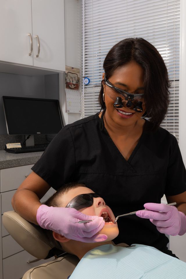 A Woman Is Examining A Child's Teeth In A Dental Office — Clinton, MD — Hamam & Lamb DDS PA