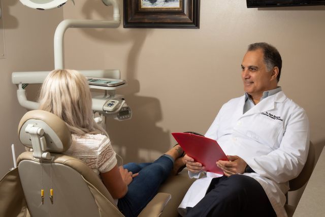 A Dentist Is Talking To A Patient In A Dental Chair While Holding A Clipboard — Clinton, MD — Hamam & Lamb DDS PA