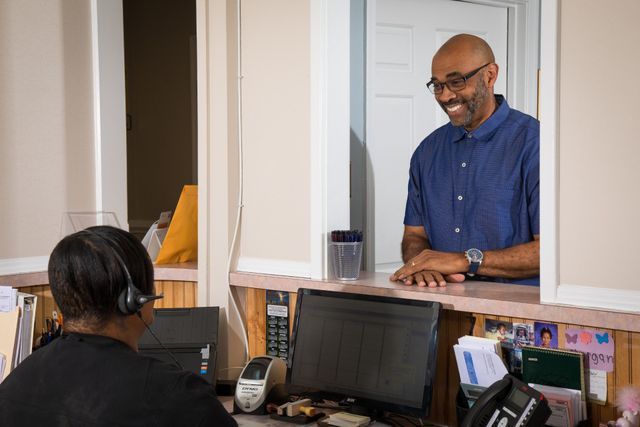 A Man Is Talking To A Woman At A Counter In A Dental Office — Clinton, MD — Hamam & Lamb DDS PA