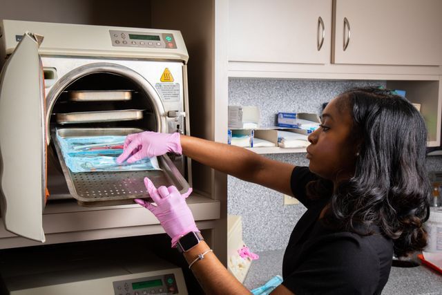A Woman Wearing Pink Gloves Is Putting A Tray Into A Machine — Clinton, MD — Hamam & Lamb DDS PA