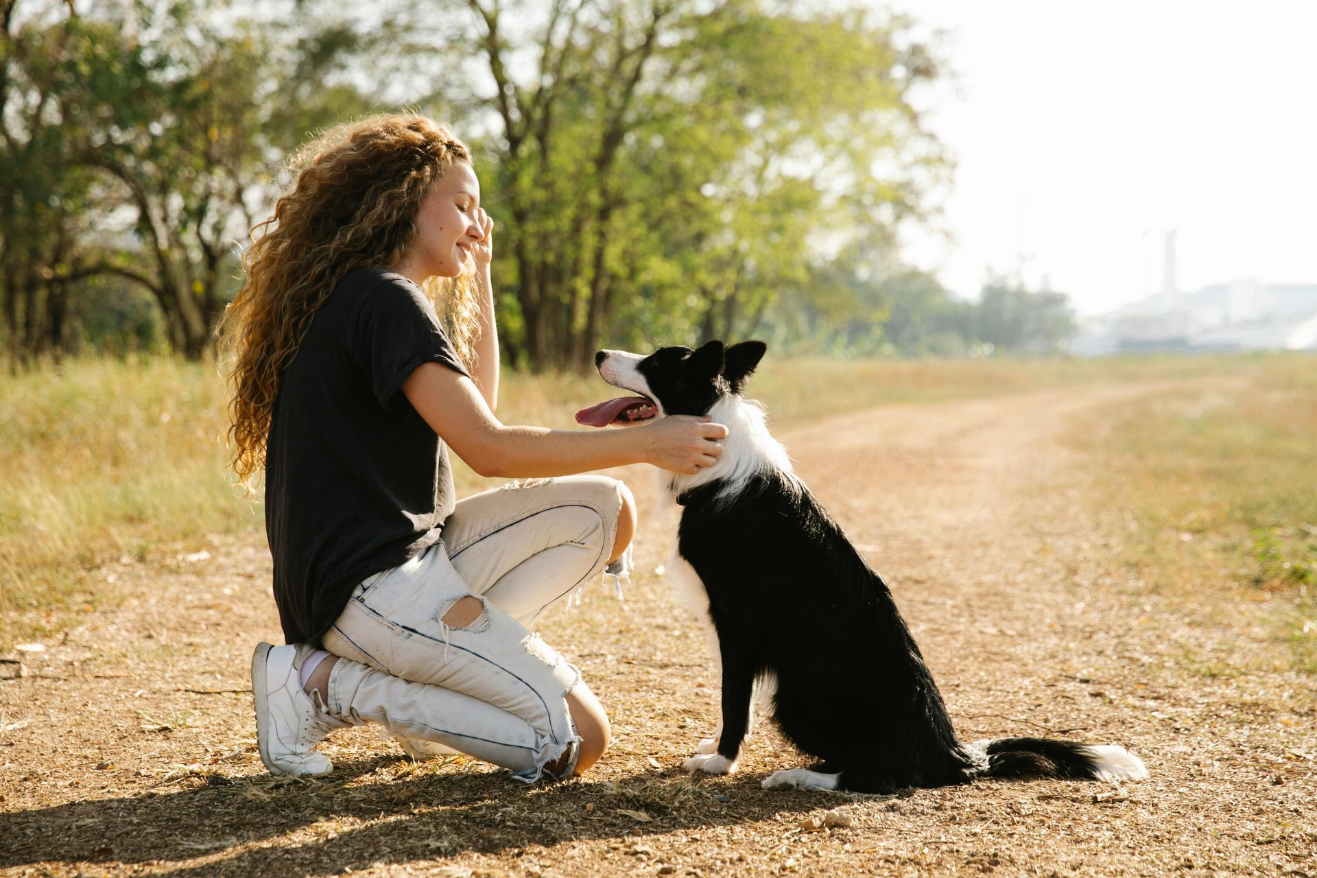 A woman is kneeling down next to a border collie dog on a dirt road.