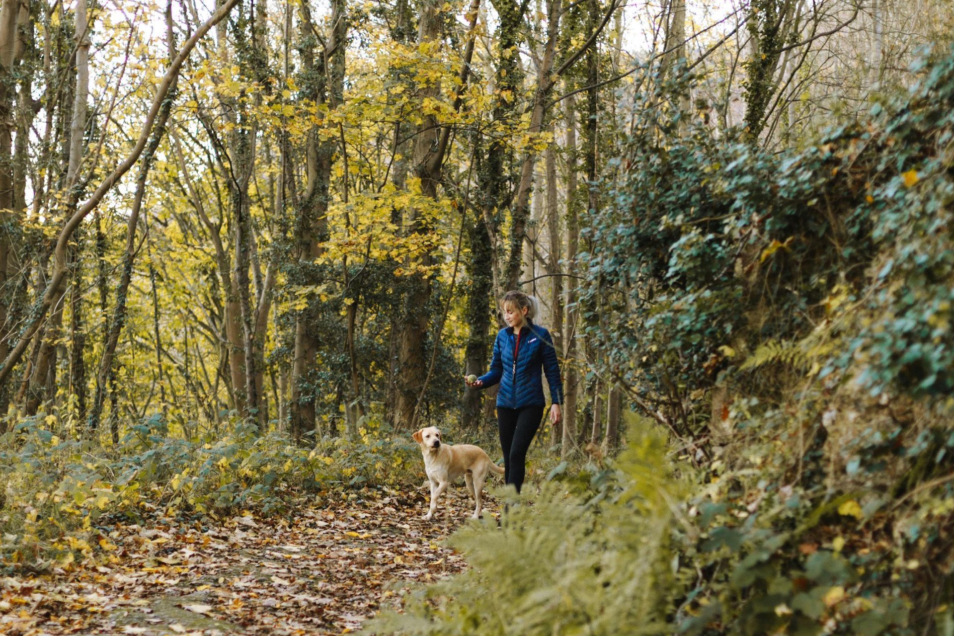 A woman is walking her dog in the woods.