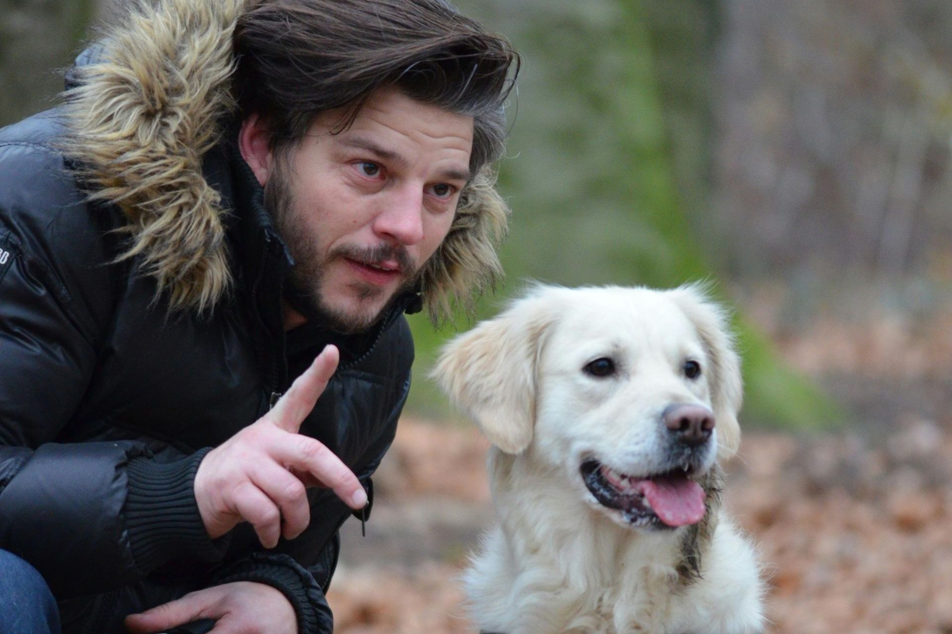 A man is kneeling down next to a white dog.