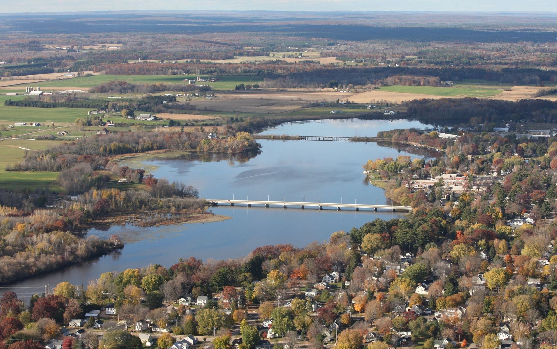 An aerial view of a bridge over a river surrounded by trees and fields.