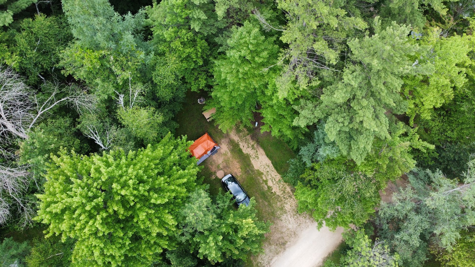 An aerial view of a tent and a car in the middle of a forest.