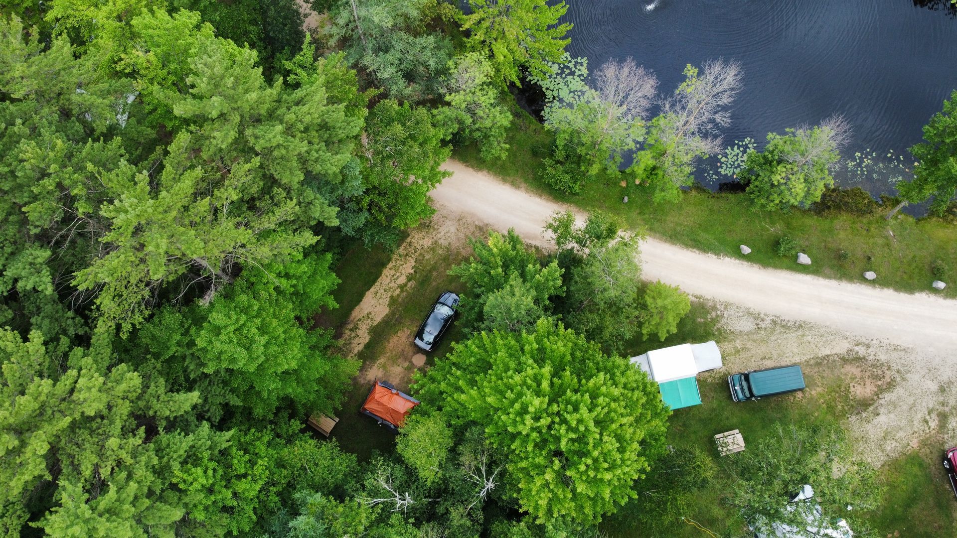 An aerial view of a dirt road surrounded by trees and a lake.