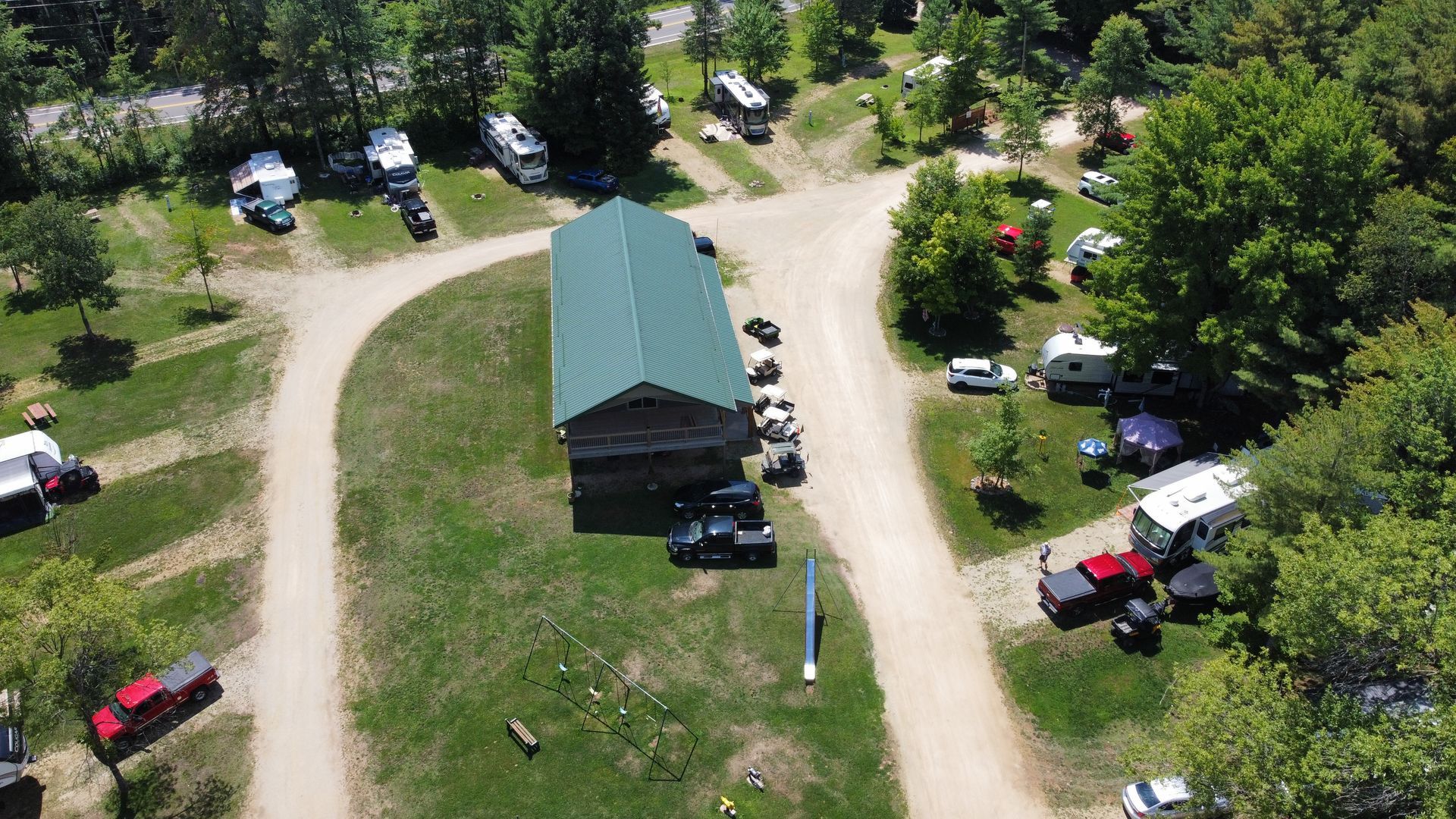 An aerial view of a campground with a green roof and a lot of vehicles parked in the grass.