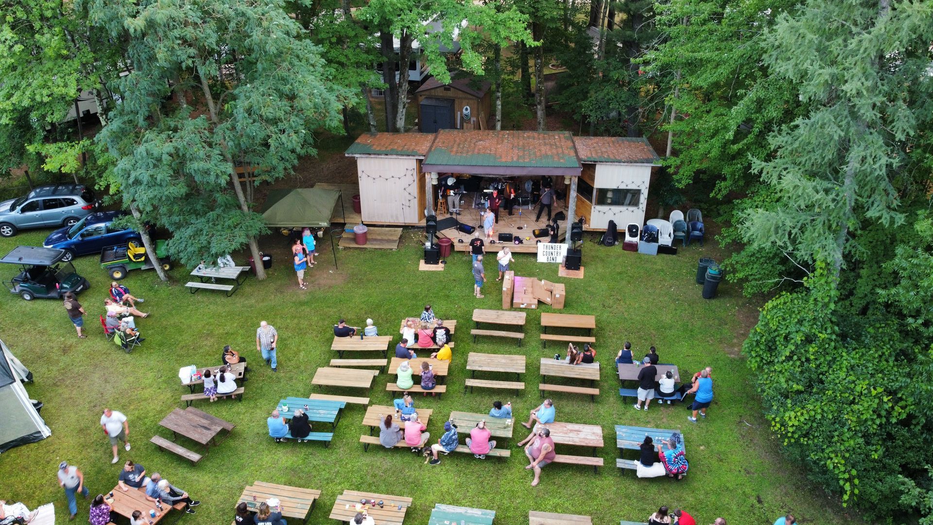 An aerial view of a group of people sitting at picnic tables in a park.