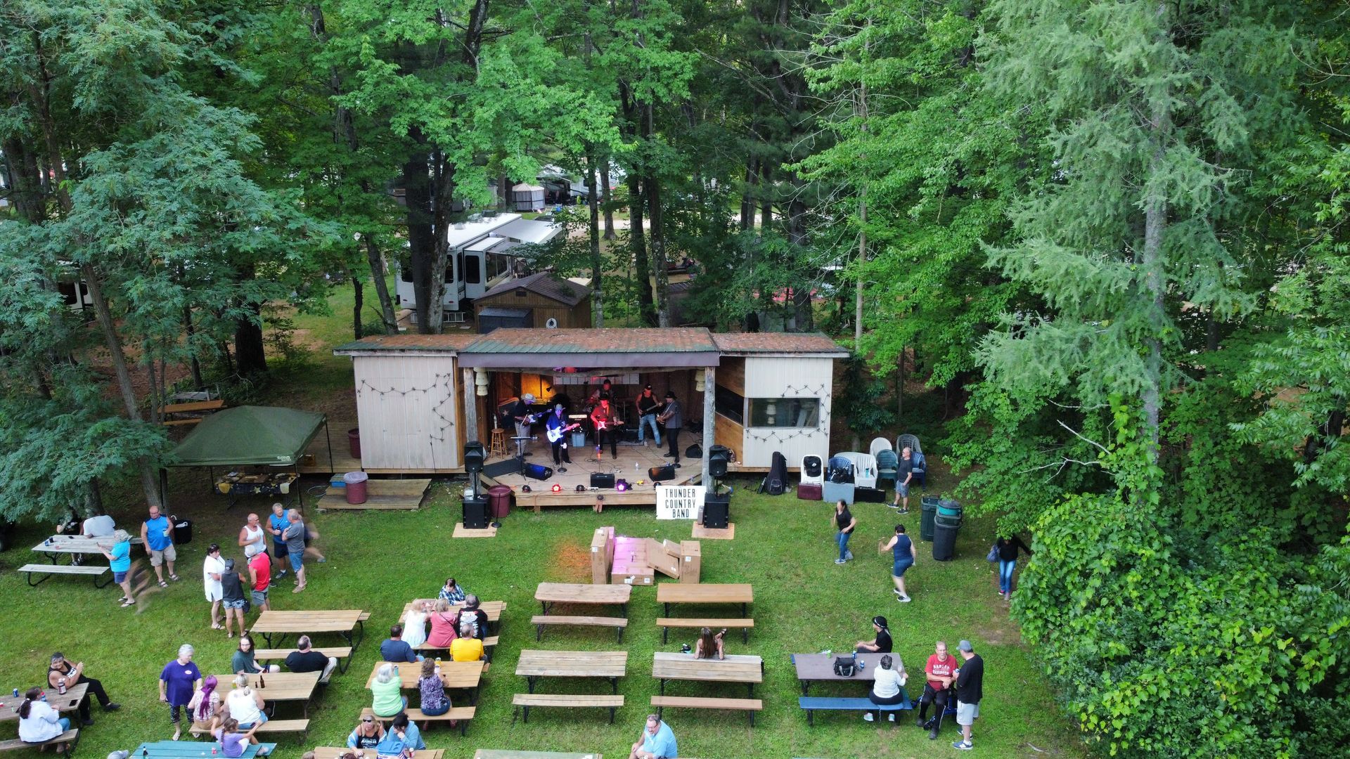 An aerial view of a group of people sitting at picnic tables in a park.