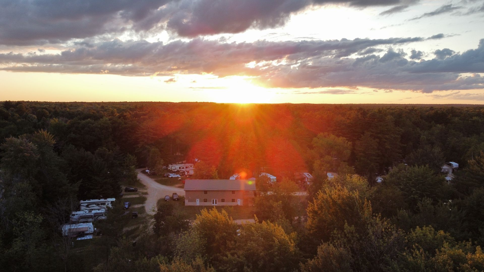 An aerial view of a sunset over a forest with a house in the foreground.