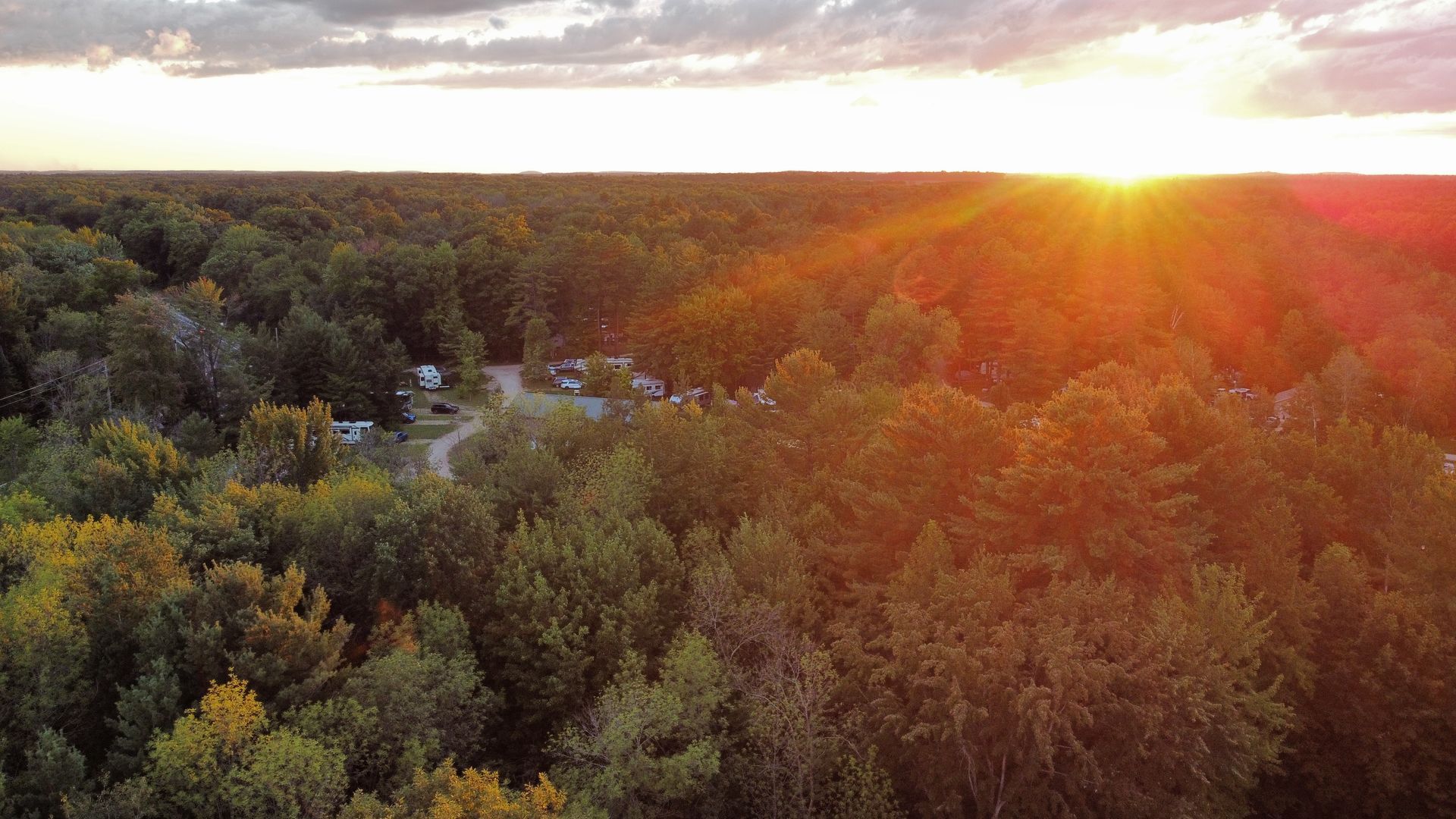 An aerial view of a forest at sunset with the sun shining through the trees.