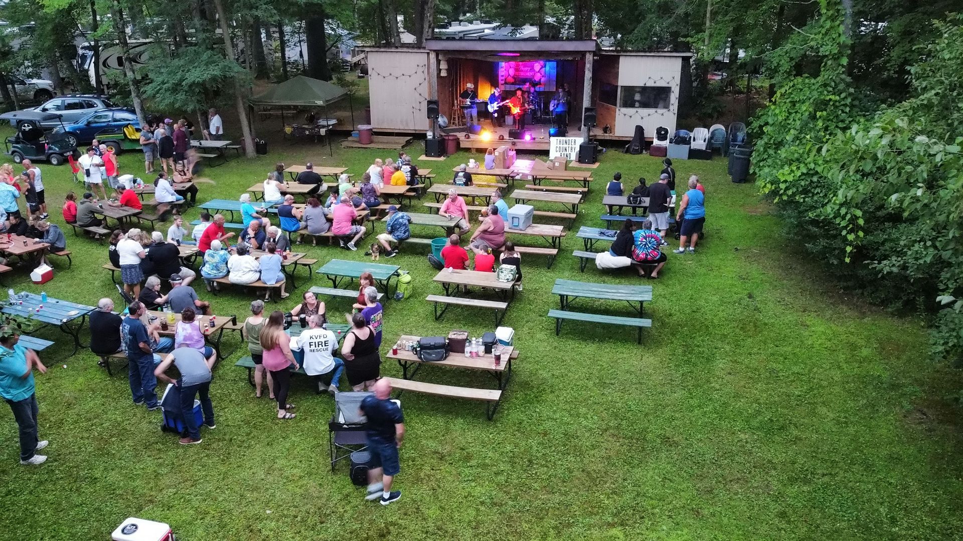 A group of people are sitting at picnic tables in a grassy field.