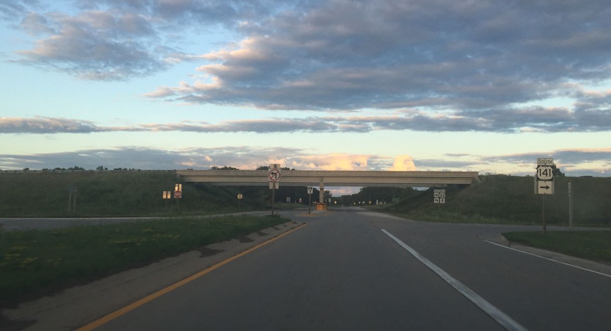 A car is driving under a bridge on a highway.