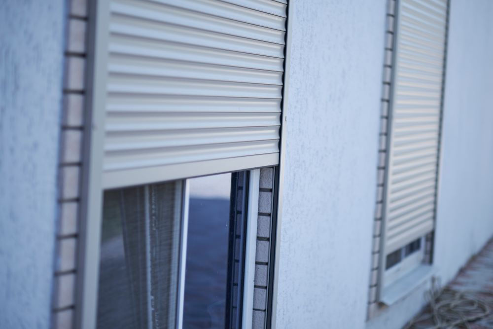 A White Building With Two Windows With Roller Shutters On Them — Maxview Blinds and Shutters in Beresfield, NSW