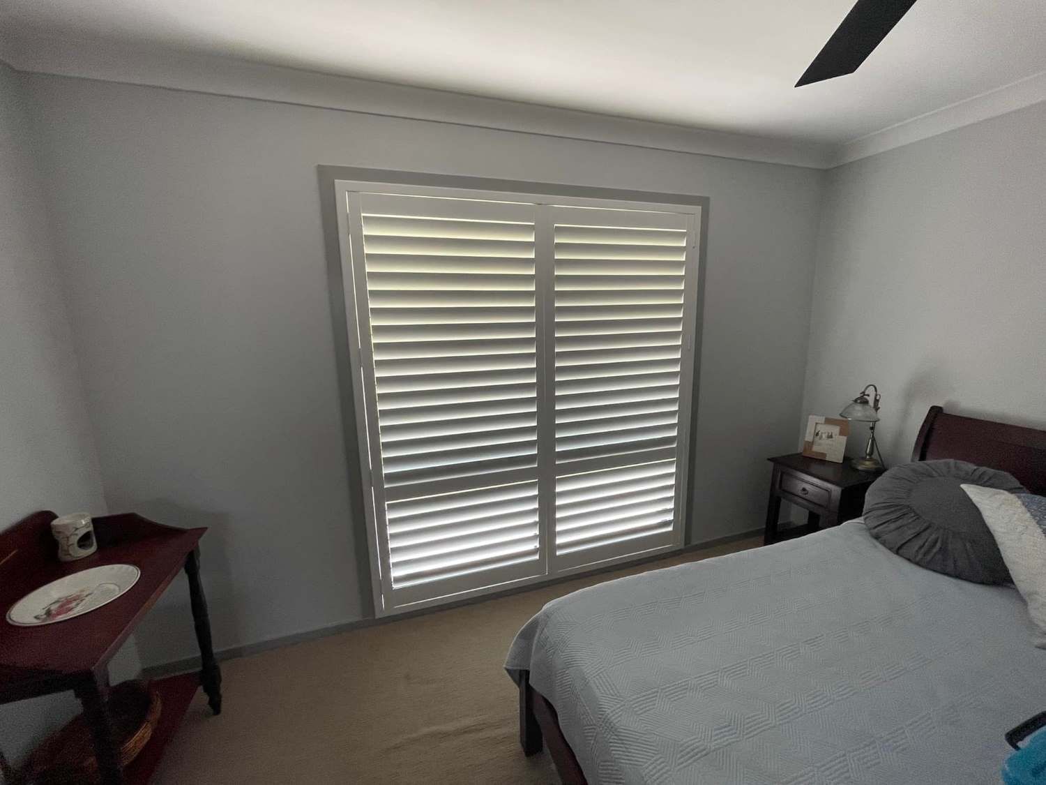 A Bedroom With A Desk And Sliding Glass Doors Fitted With Shutters — Maxview Blinds and Shutters in Beresfield, NSW