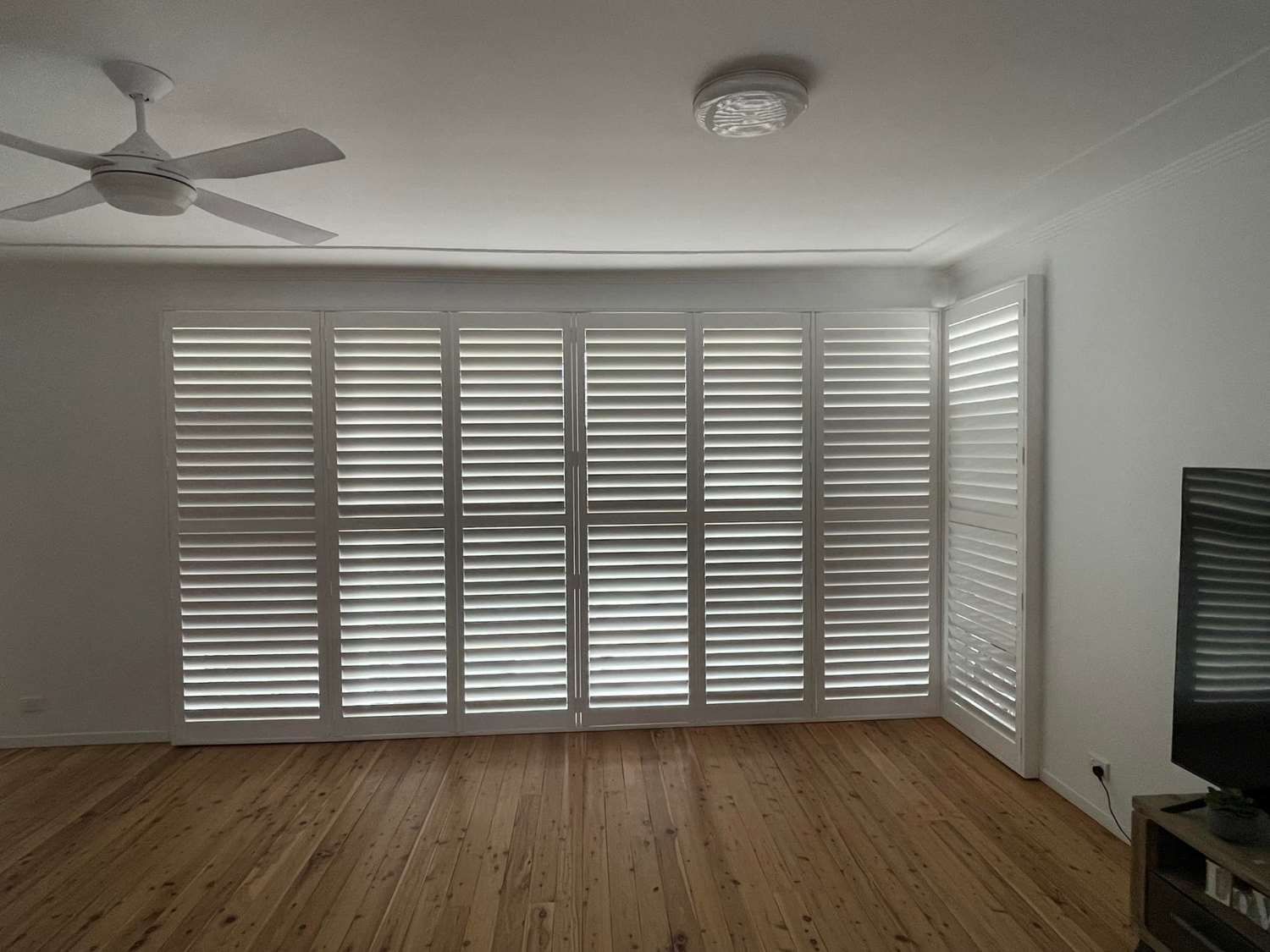 A Living Room With Window Shutters And A Ceiling Fan — Maxview Blinds and Shutters in Beresfield, NSW