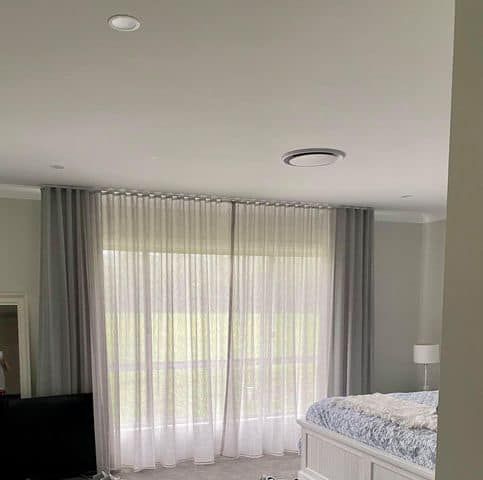 A Bedroom With A Bed, Curtains, And A Large Window — Maxview Blinds and Shutters in Beresfield, NSW