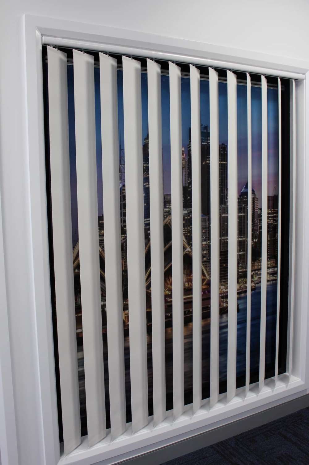 A Picture Of A City Is Behind A Window With Vertical Blinds — Maxview Blinds and Shutters in Beresfield, NSW