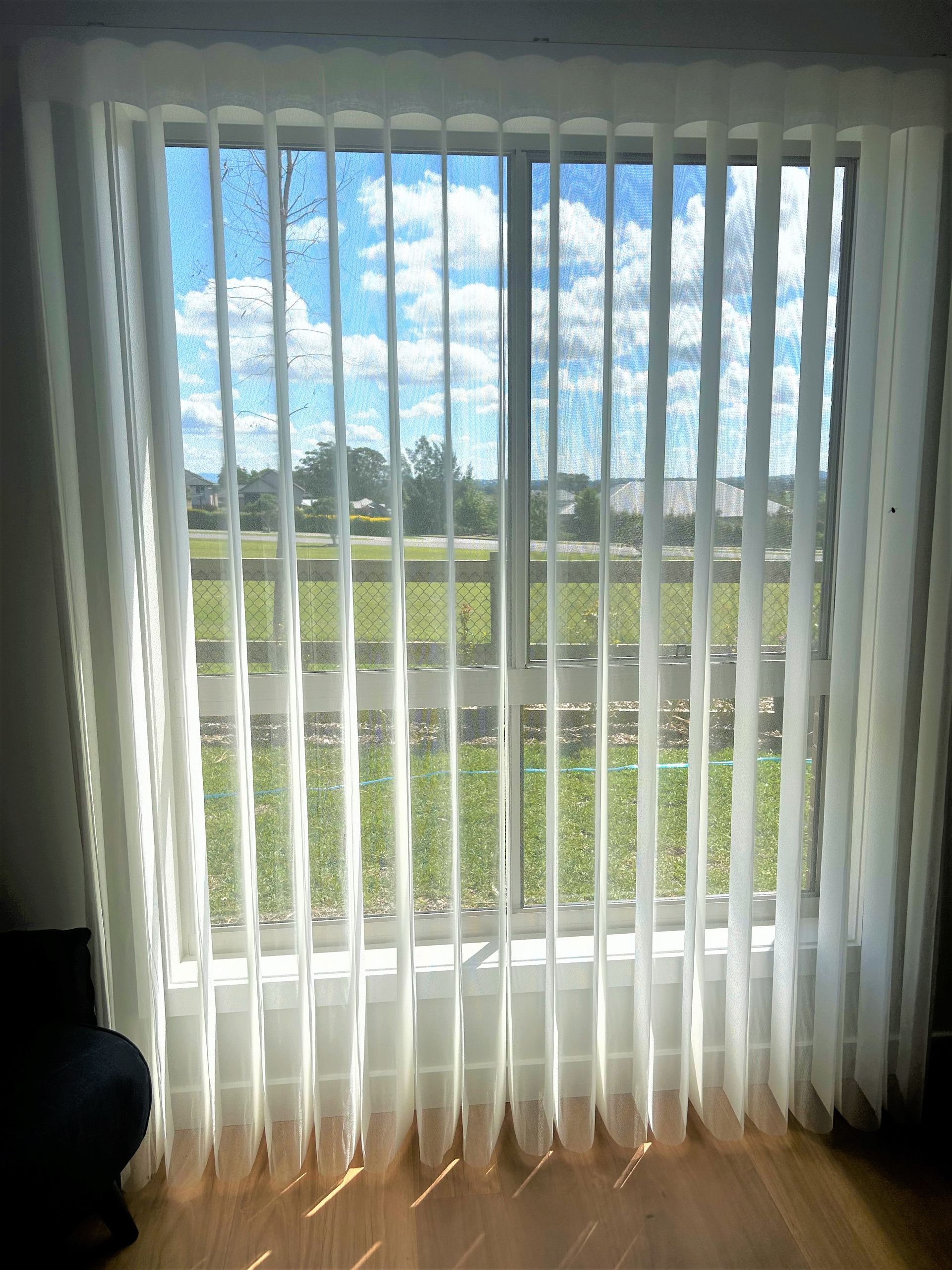 A Living Room With Two Windows Draped With Vertical White Curtains — Maxview Blinds and Shutters in Beresfield, NSW