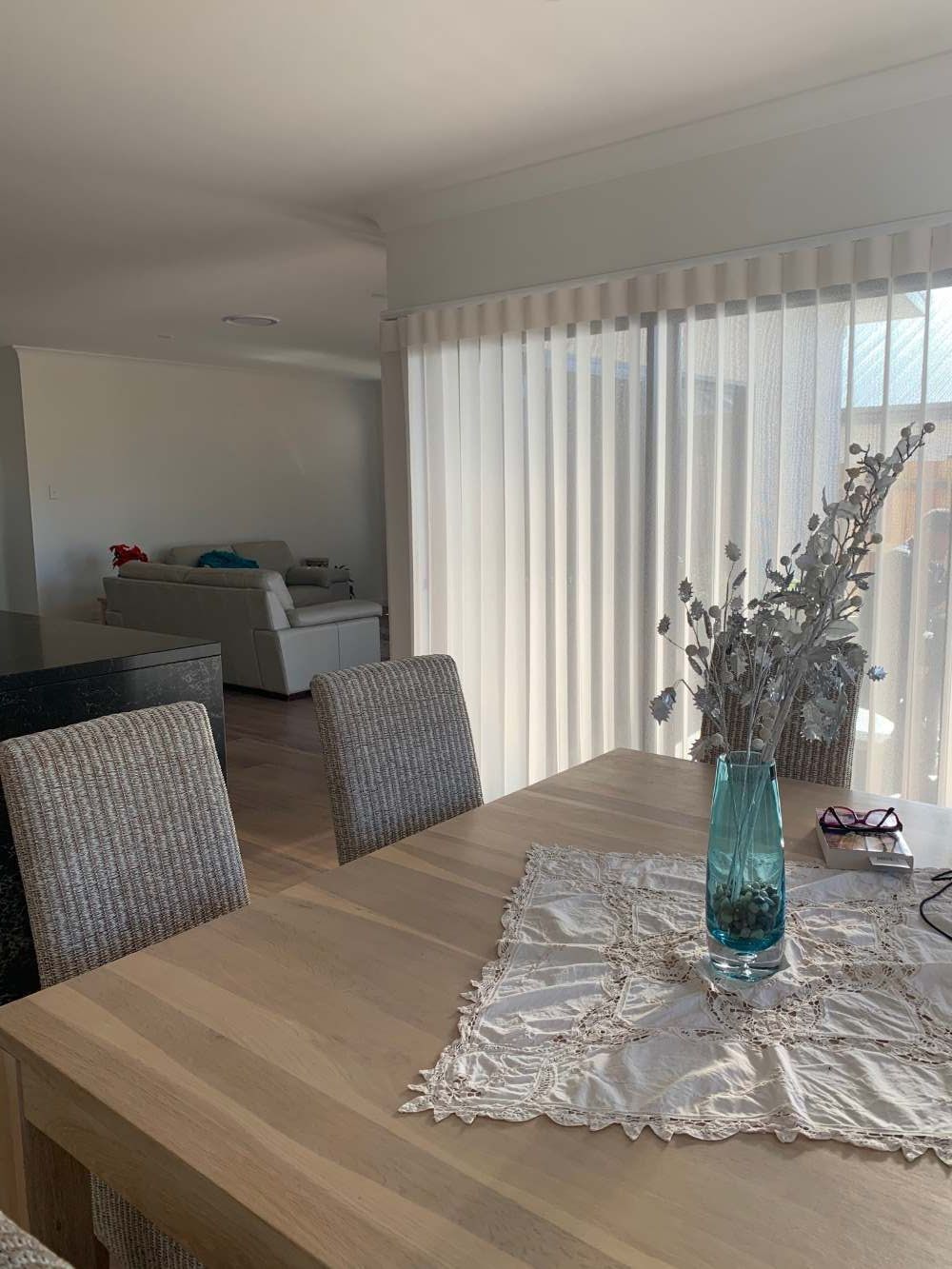 A Dining Room Table With A Vase Of Flowers And Vertical Blinds — Maxview Blinds and Shutters in Beresfield, NSW