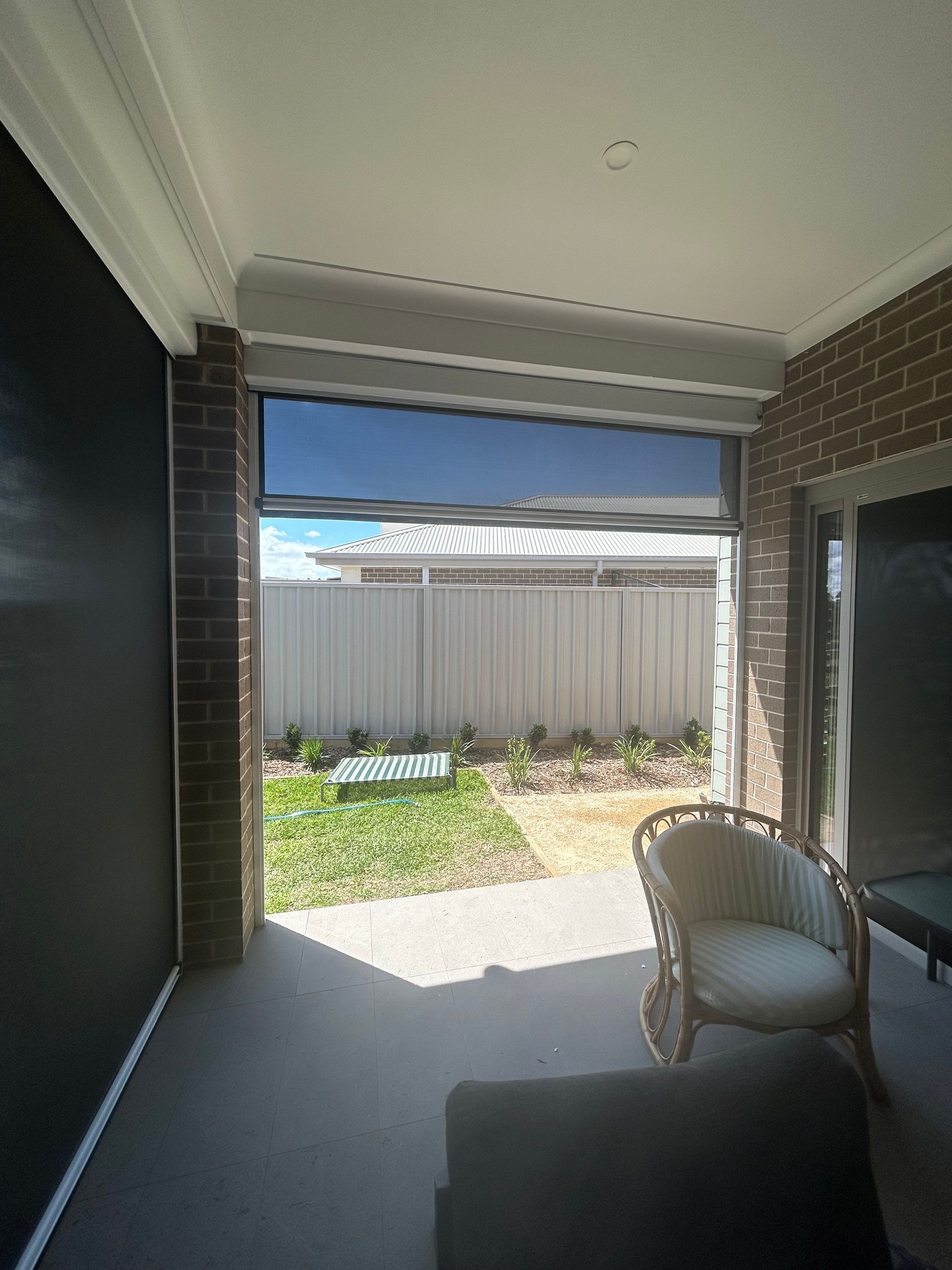 Covered patio with a Ziptrak blind, wicker chair, and view of a small backyard — Maxview Blinds and Shutters in Beresfield, NSW