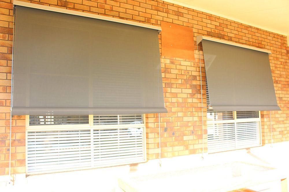 Two Windows With Gray Straight Drop Awning On A Brick Wall — Maxview Blinds and Shutters in Beresfield, NSW