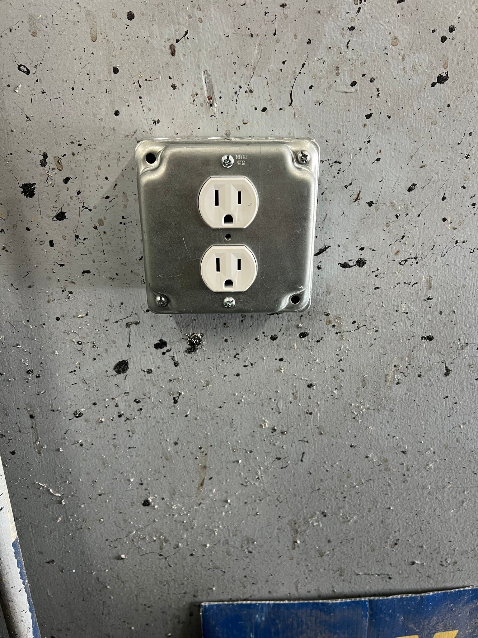 Metal electrical outlet mounted on a gray, speckled wall.