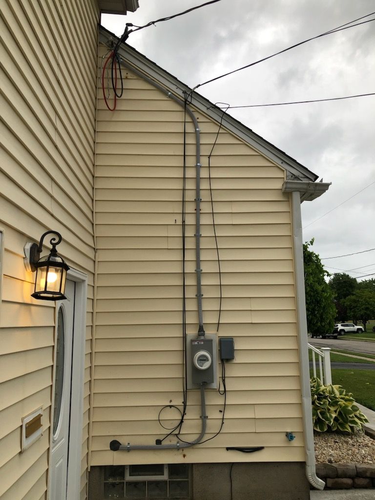 Yellow house exterior with electrical meter and conduit, wires, and a lit sconce.