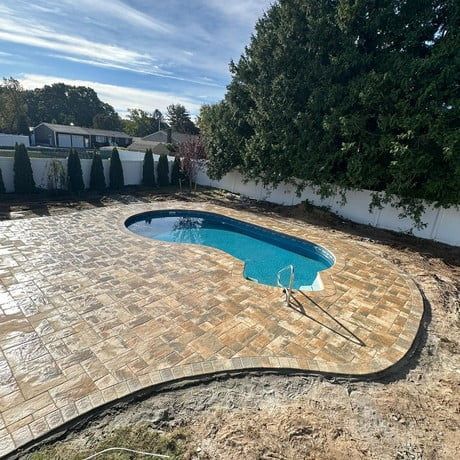 A large swimming pool is surrounded by a brick patio.