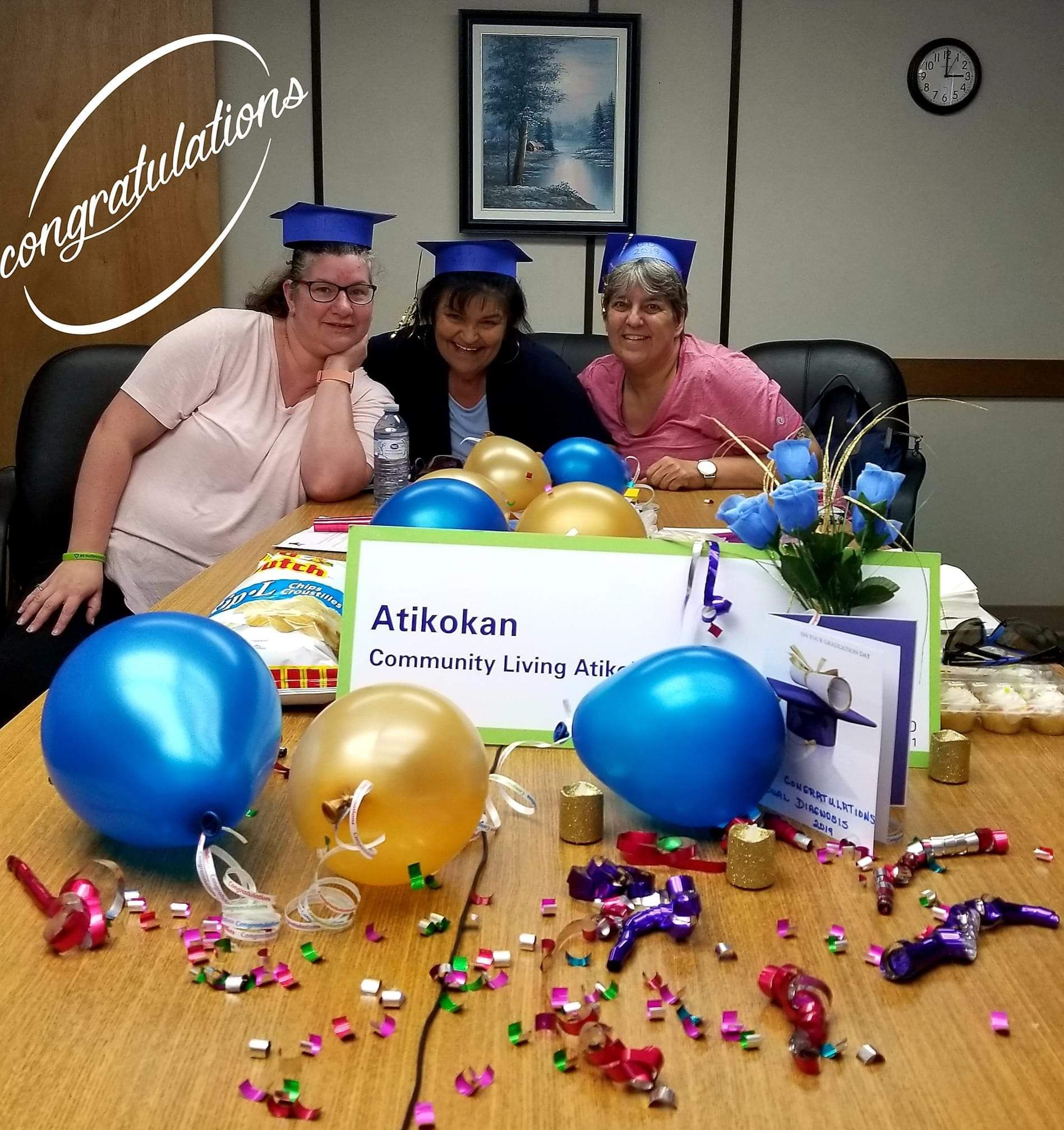 Three women sitting at a table with balloons and a sign that says congratulations
