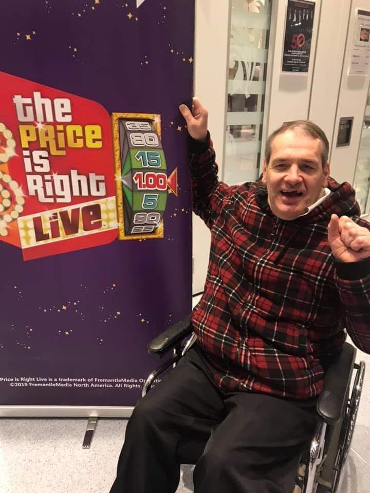 A man in a wheelchair in front of a sign that says the price is right live