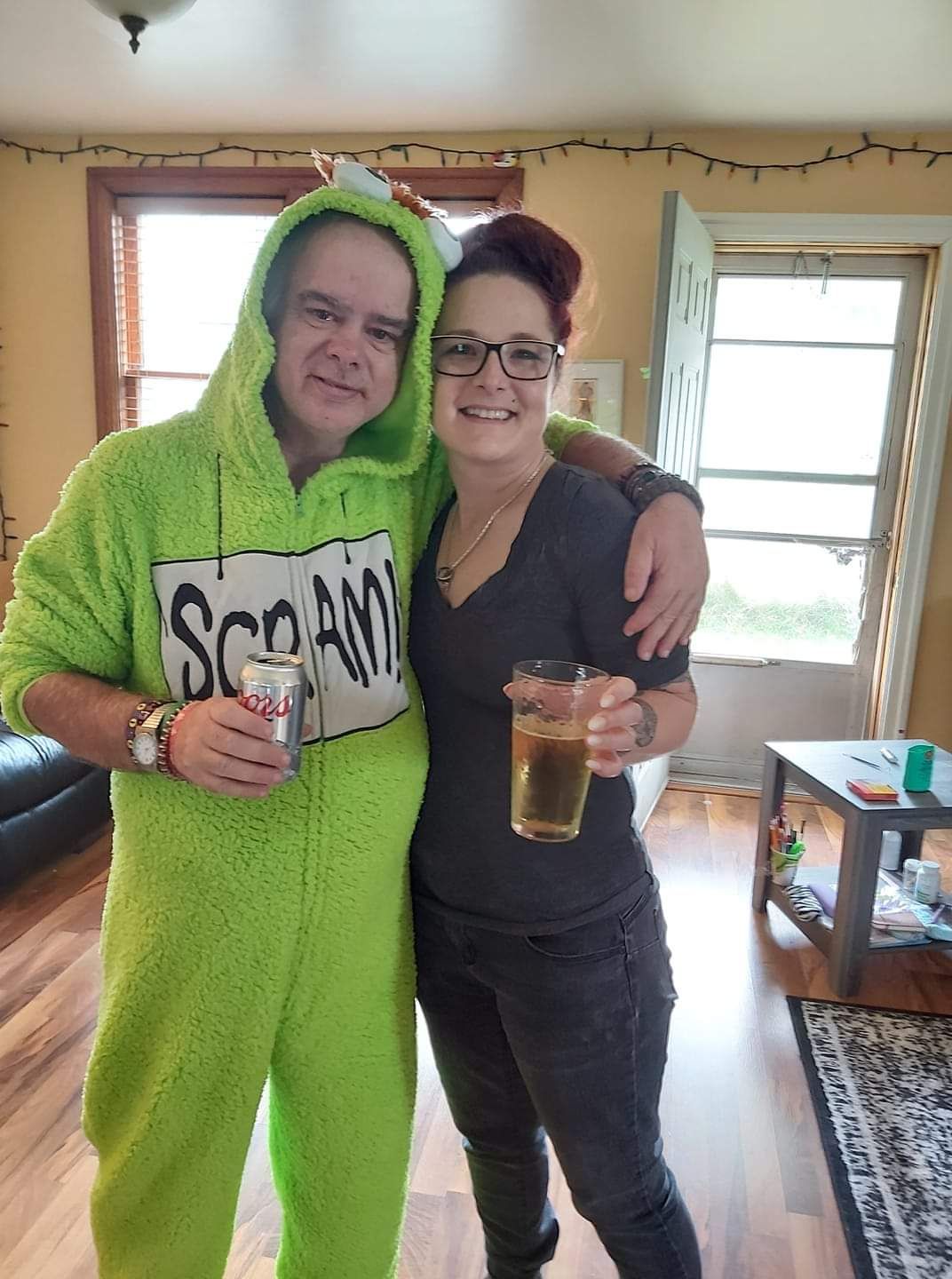 A man in a green onesie is standing next to a woman holding a glass of beer.