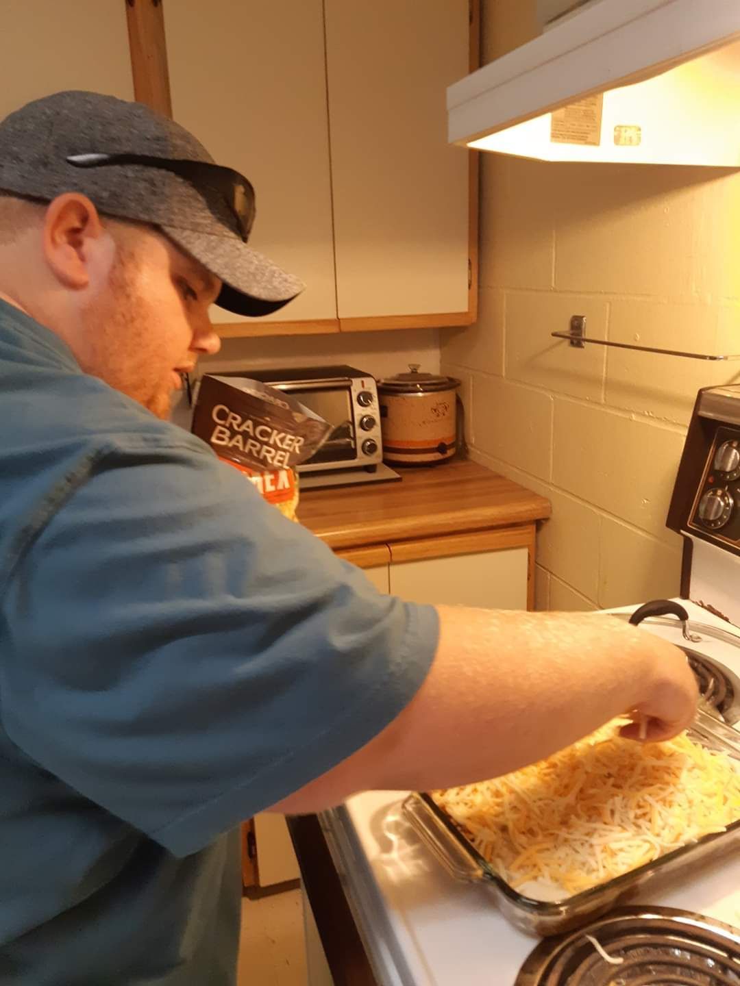 A man is cooking on a stove with a bag of crackers in the background