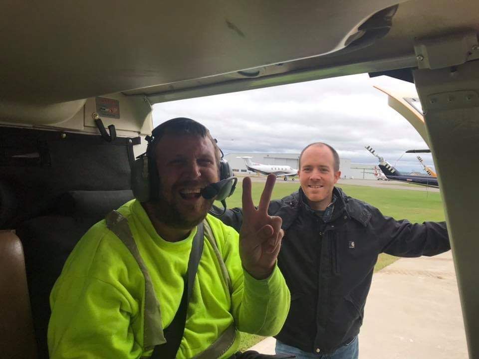 Two men are sitting in a plane giving a peace sign.