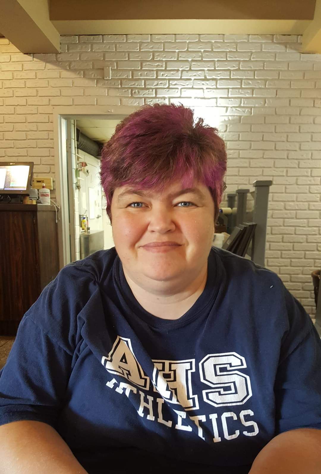 A woman with purple hair is wearing a blue shirt that says athletics.