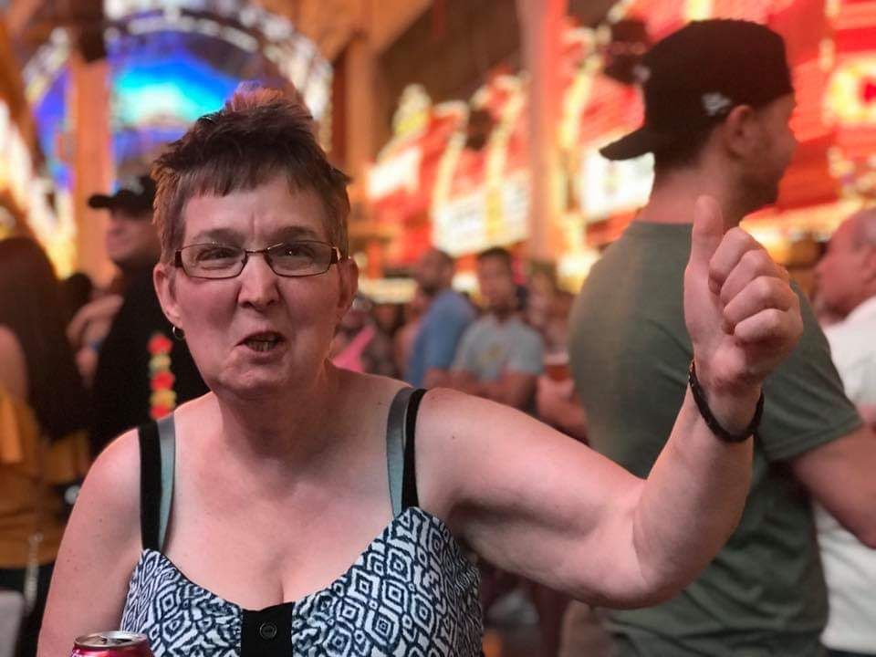 A woman is giving a thumbs up in a crowded room while holding a can of soda.