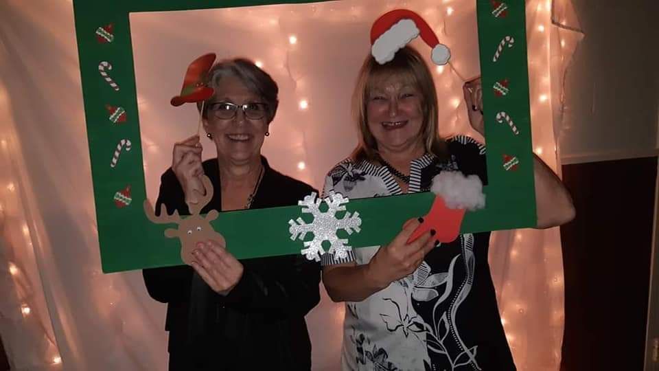 Two women are posing for a picture with a christmas photo frame.