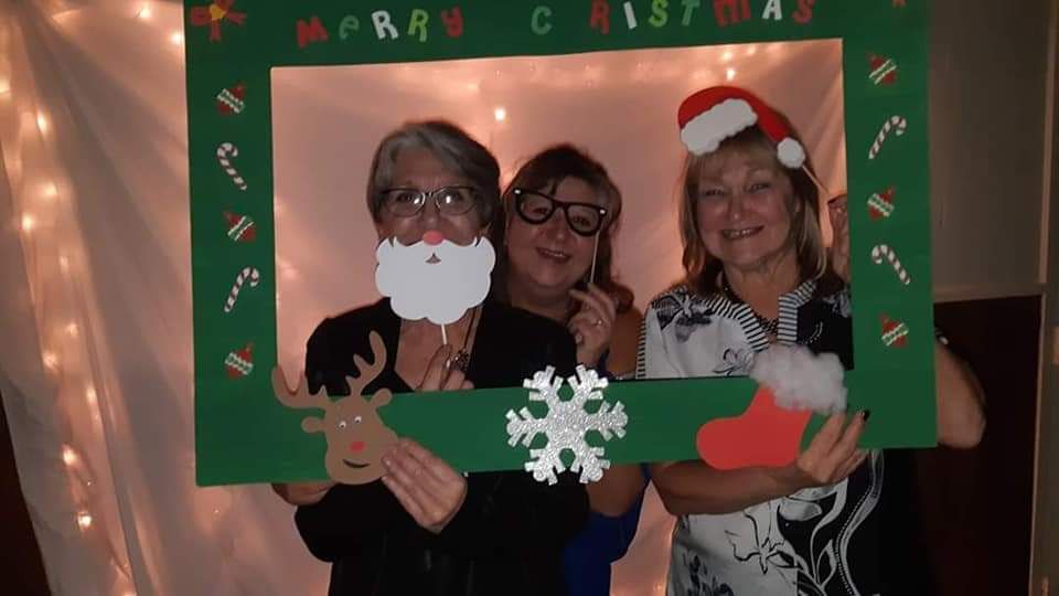 Three women are posing for a picture with a christmas frame.
