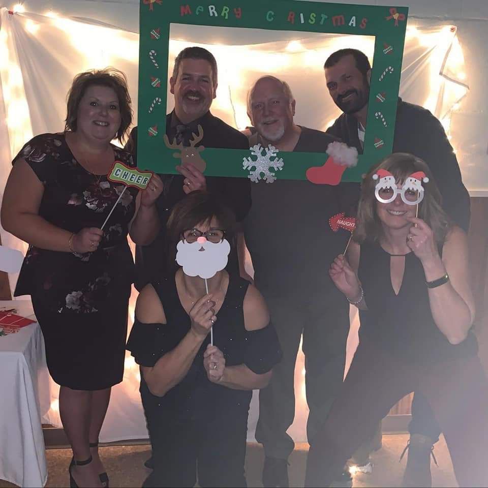 A group of people posing for a picture with a frame that says merry christmas
