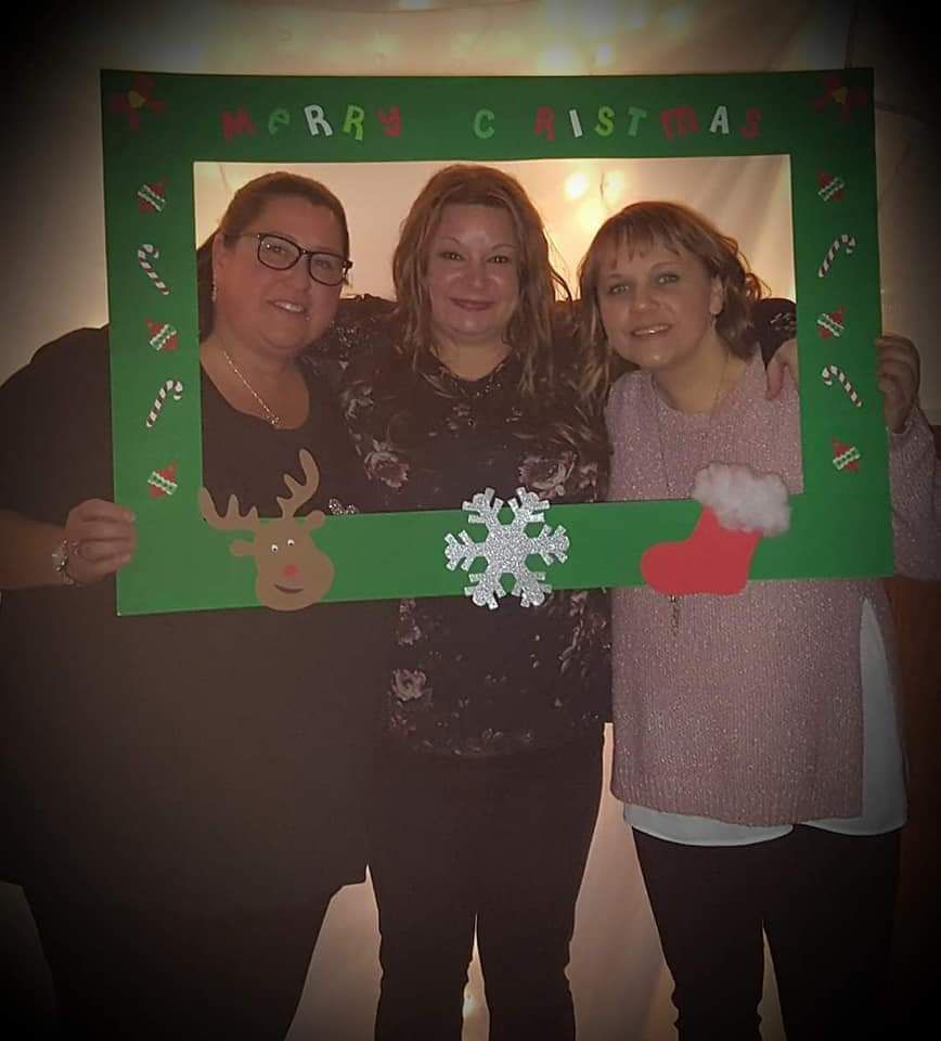 Three women are posing for a picture with a merry christmas frame