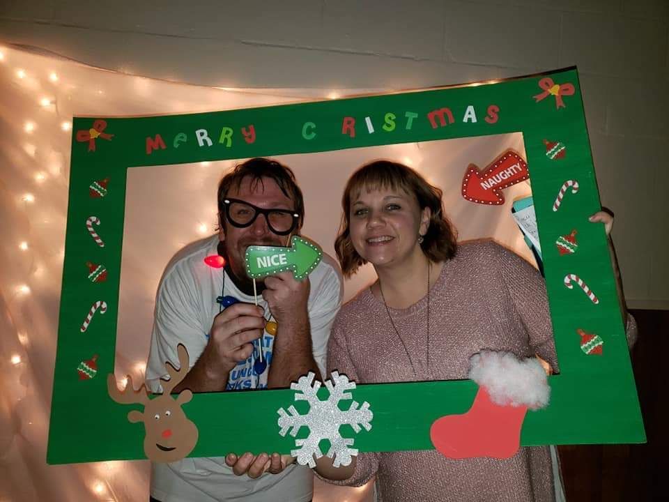 A man and a woman are posing for a picture with a christmas photo frame.