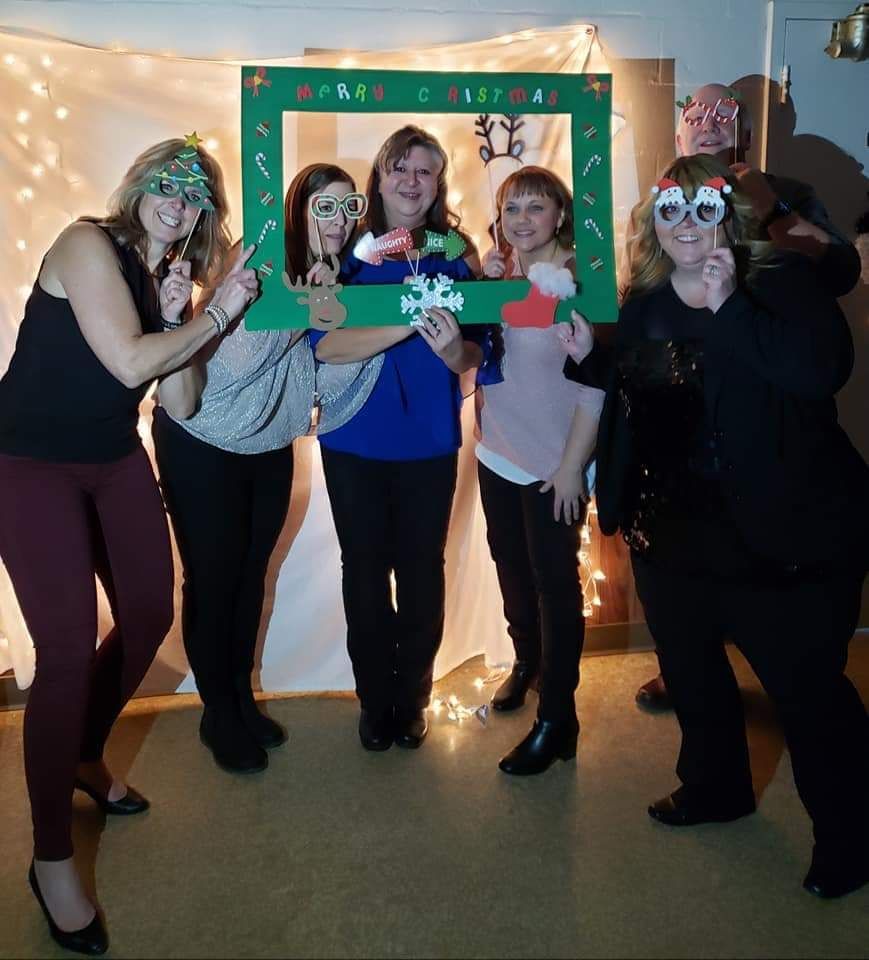 A group of women are posing for a picture with a frame that says merry christmas