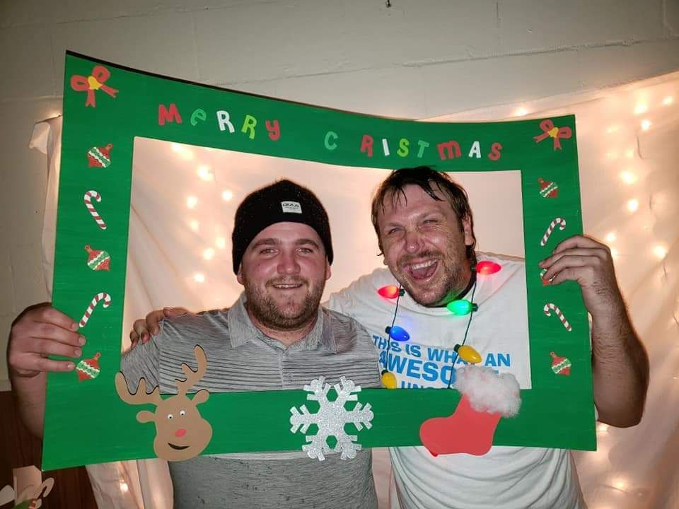 Two men are posing for a picture in a merry christmas photo frame
