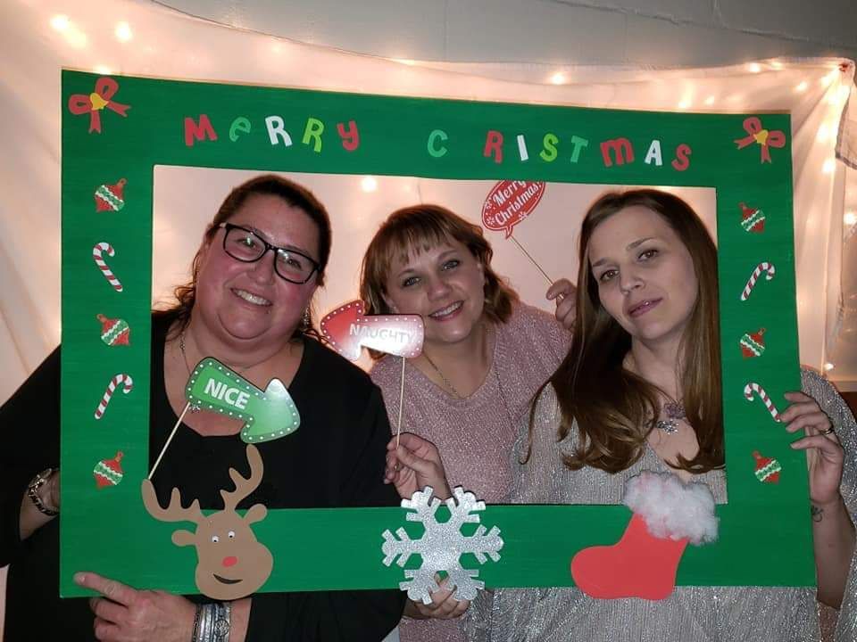 Three women are posing for a picture with a christmas photo frame.
