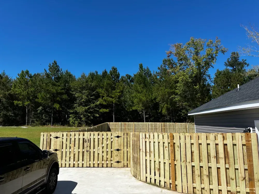 A car is parked in a driveway next to a wooden fence.