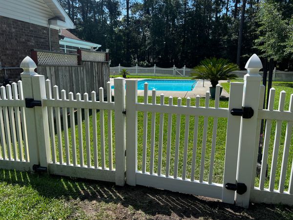 A white picket fence surrounds a swimming pool in a backyard