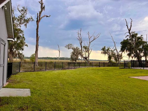 A large yard with a fence and trees in the background.