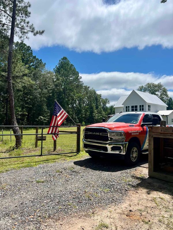 A red truck is parked in a gravel driveway in front of a house.