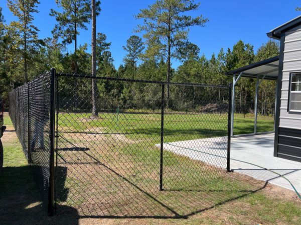 A chain link fence is surrounding a yard next to a house.