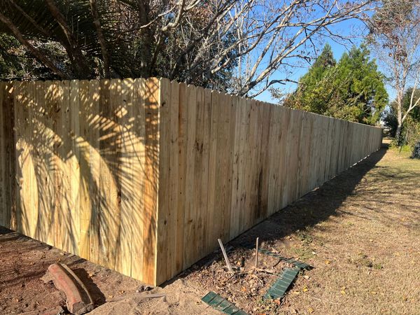 A long wooden fence is surrounded by trees in a yard.